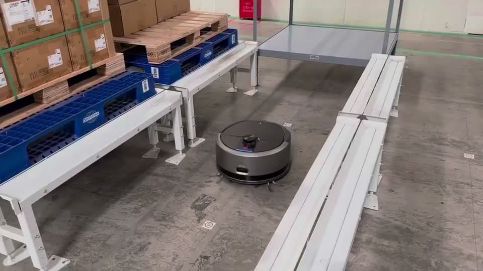 Rengjøringsrobot arbeider på et lagergulv mellom transportbaner og paller.