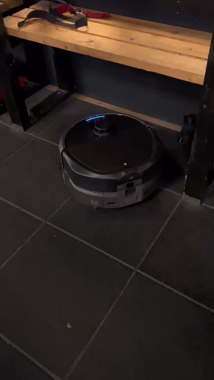 Kompakt rengjøringsrobot arbeider mellom treningsapparater på et treningssenter.